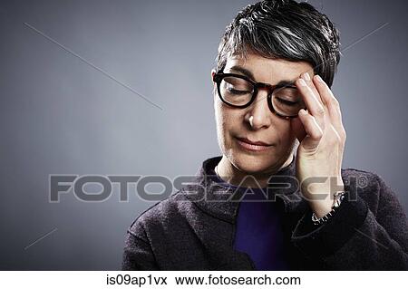 Stock Photo - Studio portrait of mature businesswoman with eyes closed and hand on forehead. Fotosearch