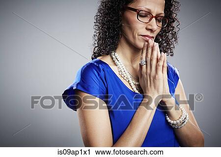 Stock Image - Studio portrait of mature woman praying. Fotosearch