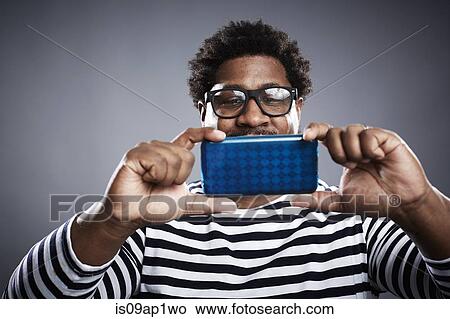Picture - Studio portrait of mid adult man taking smartphone selfie. Fotosearch