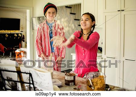 Picture - Teenage girl and brother throwing flour in kitchen. Fotosearch