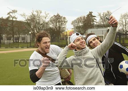Stock Photo - Three male soccer players taking celebration smartphone selfie. Fotosearch