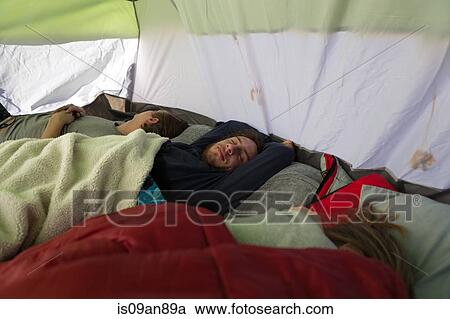 Stock Image - Three young adult friends asleep in tent. Fotosearch