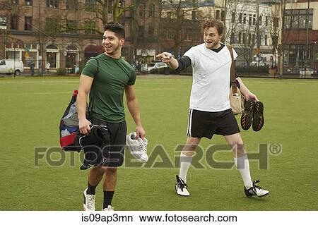 Picture - Two male soccer players carrying gym bags on soccer pitch. Fotosearch