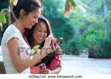 Stock Photography - "Two mid adult women looking at smartphone together, outdoors". Fotosearch