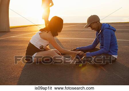 Stock Photograph - "Two women sitting on basketball court, outdoors". Fotosearch