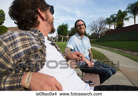 Two young male friends chatting on suburban bench View Large Photo Image Picture - Two young male friends chatting on suburban bench. Fotosearch