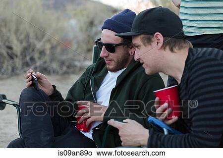 Picture - "Two young male friends looking at smartphone on campsite, Anza-Borrego Desert State Park, California, USA". Fotosearch