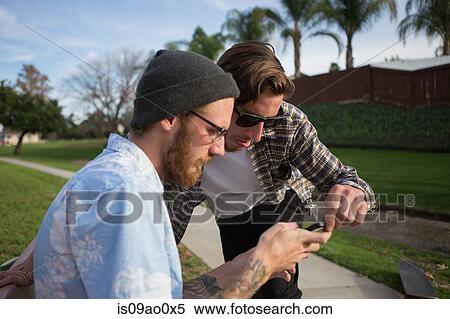 Stock Photography - Two young male friends looking at smartphone on suburban bench. Fotosearch