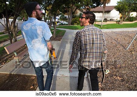 Two young male skateboarders strolling in suburban park View Large Photo Image Stock Photograph - Two young male skateboarders strolling in suburban park. Fotosearch