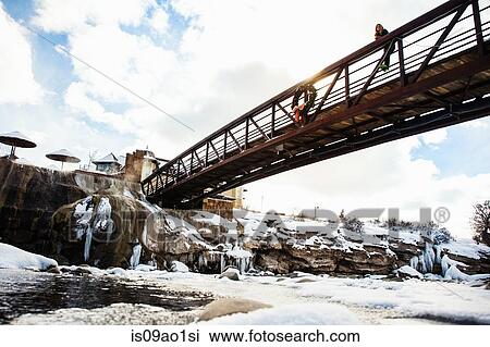 Stock Image - "Woman looking out from river footbridge, Pagosa Springs, Colorado, USA". Fotosearch