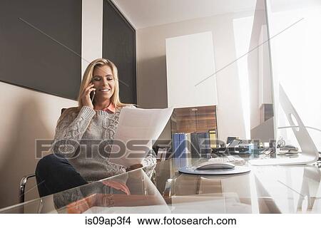 Picture - Young businesswoman chatting on smartphone whilst reading notes. Fotosearch