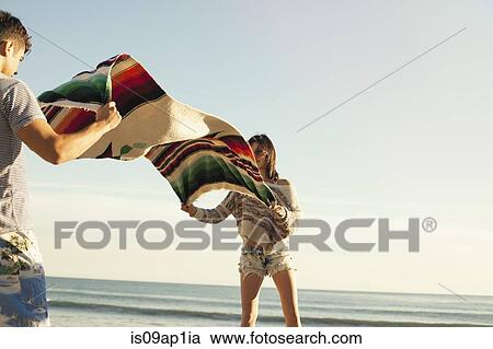 "Young couple at beach, shaking out picnic blanket" View Large Photo Image Stock Image - "Young couple at beach, shaking out picnic blanket". Fotosearch