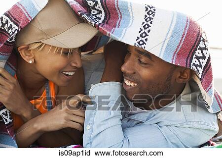 Stock Image - Young couple laughing together under picnic blanket. Fotosearch