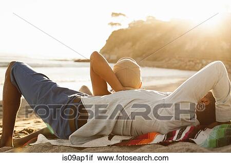 Stock Image - "Young couple lying together on beach, rear view". Fotosearch