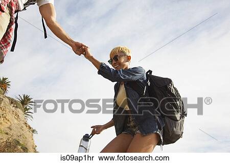 Stock Photography - "Young couple on trek together, man helping woman". Fotosearch