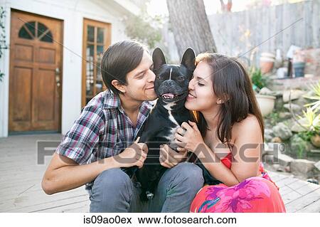 Stock Photo - Young couple sitting on patio snuggling up to dog. Fotosearch