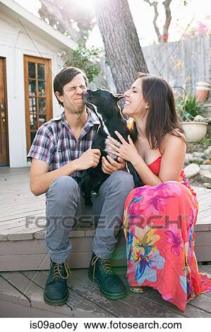 Young couple sitting on patio with dog licking face View Large Photo Image Stock Photo - Young couple sitting on patio with dog licking face. Fotosearch