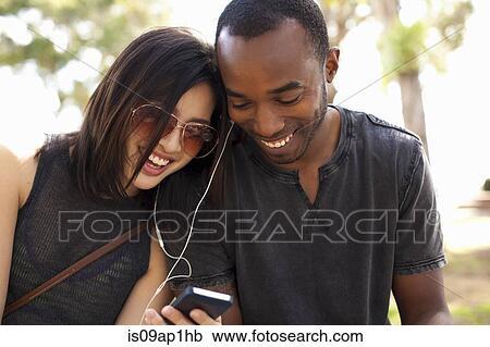 Stock Image - "Young couple sitting together, sharing earphones". Fotosearch