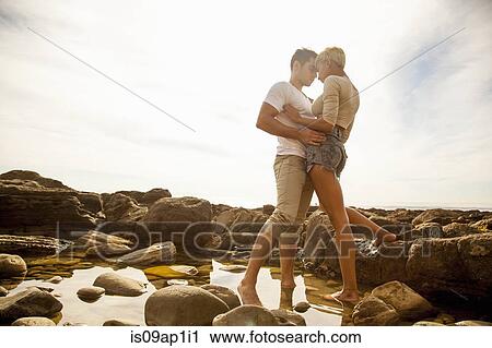 Stock Image - "Young couple standing together, face to face, in rock pool on beach". Fotosearch