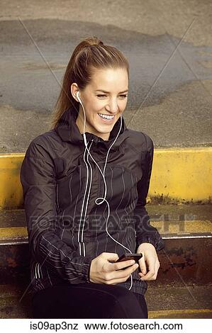 Young female runner listening to music on earphones View Large Photo Image Stock Photo - Young female runner listening to music on earphones. Fotosearch