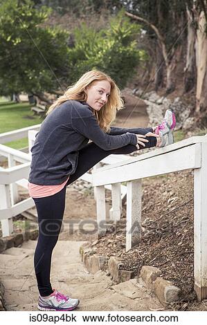 Stock Image - Young female runner warming up on park stairway. Fotosearch