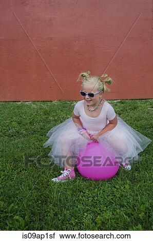 Stock Image - "Young girl wearing tutu, bouncing on pink inflatable hopper". Fotosearch