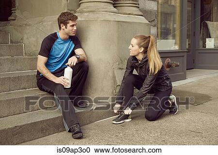Stock Image - Young male and female runners preparing for run on sidewalk. Fotosearch
