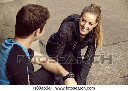Stock Image - Young male and female runners tying shoelace on sidewalk. Fotosearch