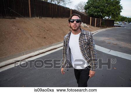 Young male hipster looking at camera whilst walking on suburban road View Large Photo Image Stock Image - Young male hipster looking at camera whilst walking on suburban road. Fotosearch
