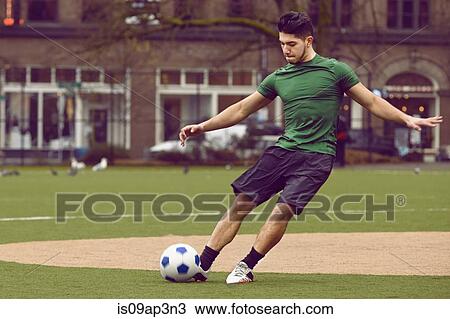 Stock Image - Young male soccer player kicking ball on soccer pitch. Fotosearch