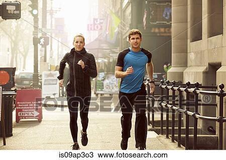 Stock Image - "Young man and woman running along street, Pioneer Square, Seattle, USA". Fotosearch