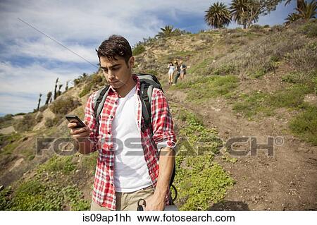 "Young man at bottom of hill, using smartphone, friends trailing behind" View Large Photo Image Stock Image - "Young man at bottom of hill, using smartphone, friends trailing behind". Fotosearch