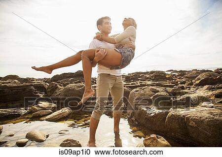 Young man carrying girlfriend across rock pool on beach View Large Photo Image Stock Image - Young man carrying girlfriend across rock pool on beach. Fotosearch