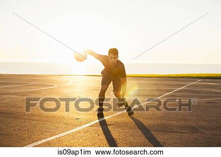 Picture - "Young man, dribbling basketball on court, outdoors". Fotosearch