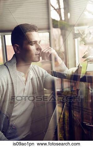 Picture - Young man gazing out of living room window. Fotosearch