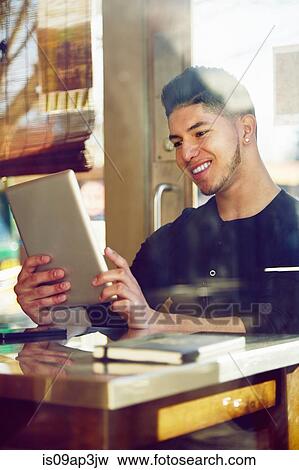 Stock Photo - Young man in cafe using digital tablet. Fotosearch