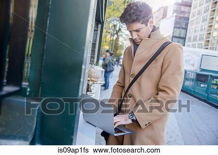 Stock Photograph - "Young man in street, using laptop". Fotosearch