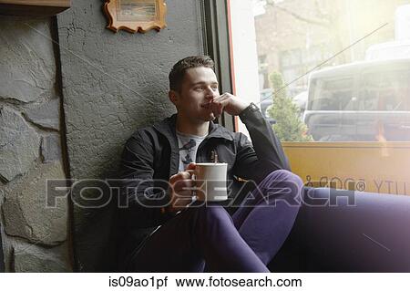 Young man sitting in cafe window seat looking out of window View Large Photo Image Stock Image - Young man sitting in cafe window seat looking out of window. Fotosearch