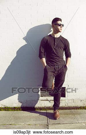 Young man standing by white wall View Large Photo Image Stock Photograph - Young man standing by white wall. Fotosearch