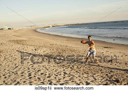 Stock Image - Young man throwing ball on beach. Fotosearch