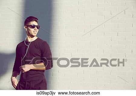 Stock Photo - Young man wearing sunglasses by white wall. Fotosearch