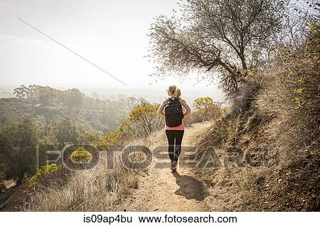 Stock Photograph - Young woman hiking along dirt track. Fotosearch