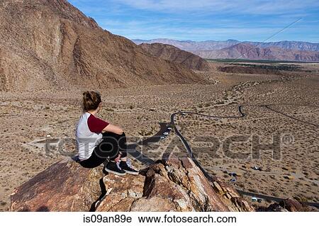 Stock Image - "Young woman looking out at view from rocks, Anza-Borrego Desert State Park, California, USA". Fotosearch
