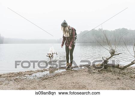 Picture - Young woman playing with her dog on misty lakeside. Fotosearch