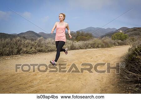 Stock Photograph - Young woman running down dirt track. Fotosearch