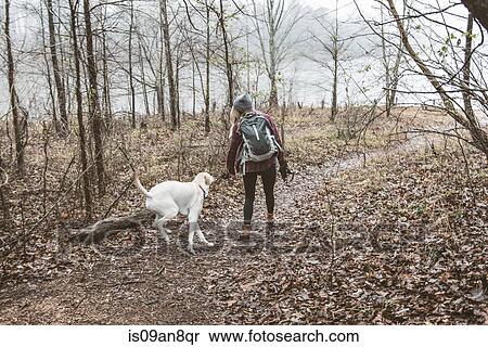 Stock Photography - Young woman walking her dog in lakeside forest. Fotosearch