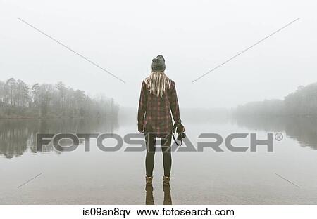 Young woman with camera standing in misty lake View Large Photo Image Stock Photo - Young woman with camera standing in misty lake. Fotosearch