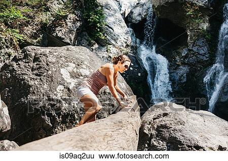 A woman climbing on rock near a waterfall View Large Photo Image Stock Photograph - A woman climbing on rock near a waterfall. Fotosearch