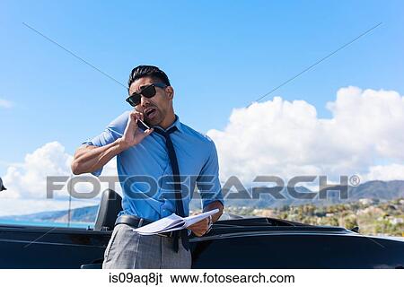 Stock Photograph - Anxious young businessman at coast parking lot talking on smartphone. Fotosearch