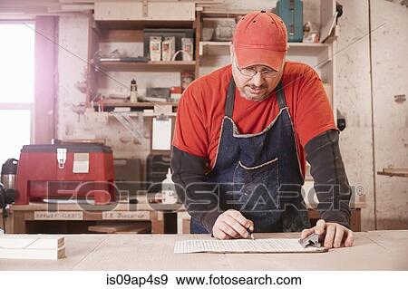 Cabinet maker checking blueprint at workshop bench View Large Photo Image Stock Photo - Cabinet maker checking blueprint at workshop bench. Fotosearch